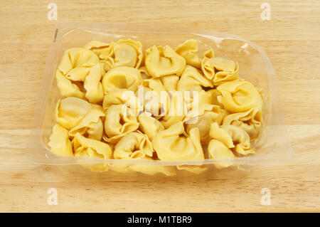 Raw tortelloni Nudeln in einem Kunststoff Karton auf Holz Schneidebrett Stockfoto