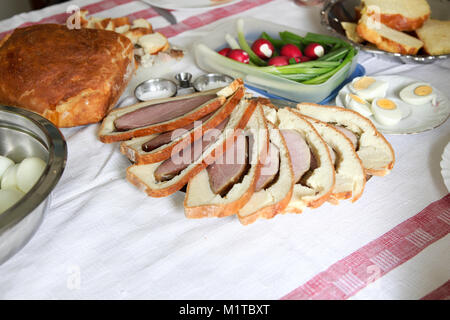 Ostern Tisch mit Eiern, Schinken im Brotteig, hausgemachtes Brot, Radieschen und junge Bug Stockfoto