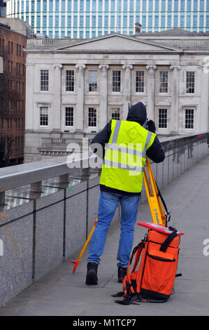 Ein Bauarbeiter oder Ingenieur Mess- Gebäude und Strukturen mit einem theodolit auf einem gelben Stativ. Ein Gutachter in Hohe Sichtbarkeit Weste arbeiten Stockfoto