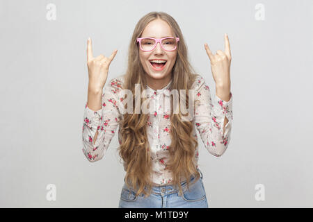 Glück junge erwachsene Mädchen, Rock und Roll Finger und Kamera mit verrückt aussehen. Studio shot, auf grauem Hintergrund Stockfoto