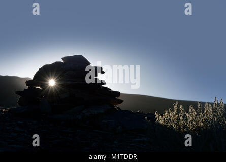 Schwarze Silhouette der Buddhistischen Stupa handgearbeitet aus Steinen, stehend auf einem Berghang, im Hintergrund einer Sonnenuntergang, auf der rechten ein Bush von Berg sa Stockfoto