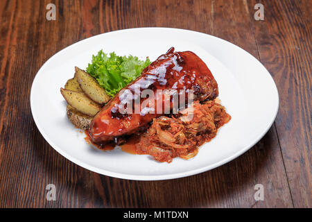 Auf dem Tisch ist eine Platte von gegrillten Rippchen, Sauerkraut, gebackene Kartoffeln und Salat letuk Stockfoto