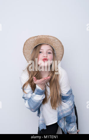 Mädchen bläst einen Kuss in Blue Plaid Shirt und Strohhut auf weißem Hintergrund Stockfoto