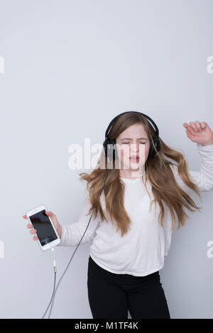 Mädchen singen mit Leidenschaft, mit geschlossenen Augen Hören von Musik auf dem Smartphone mit Ohrbügel Kopfhörer auf weißem Hintergrund, vorsätzliche Bewegungsunschärfe Stockfoto
