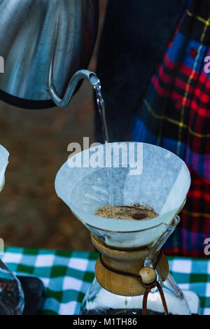 Barista gießt kochendes Wasser fron spezialisierte Wasserkocher auf Gießen über Kaffee in artisan Glas Brewer, während draußen Stockfoto