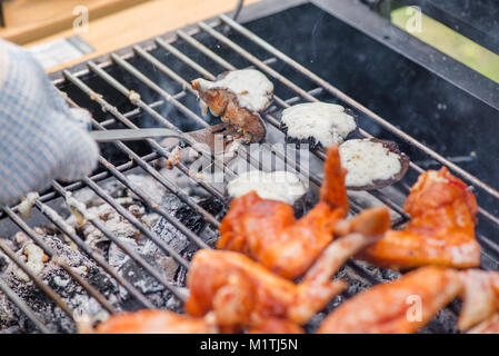 Champignons mit Käse und Chicken Wings am Grill zubereitet auf heiße Holzkohle und Feuer. Würzig mariniertes Hähnchenfleisch Kochen über dem Feuer. Stockfoto