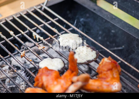 Champignons mit Käse und Chicken Wings am Grill zubereitet auf heiße Holzkohle und Feuer. Würzig mariniertes Hähnchenfleisch Kochen über dem Feuer. Stockfoto