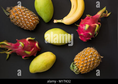 Tropische Früchte Ananas, Banane, Dragon Obst und Mango auf schwarzem Hintergrund. Ansicht von oben. Flach. Stockfoto