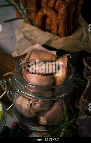 Vertikale Foto mit mehreren braun Knoblauchzehen, die in Glas Glas sind. Das Glas ist voll von Gemüse. Dahinter ist der Jahrgang kann mit Papier innen und Stockfoto