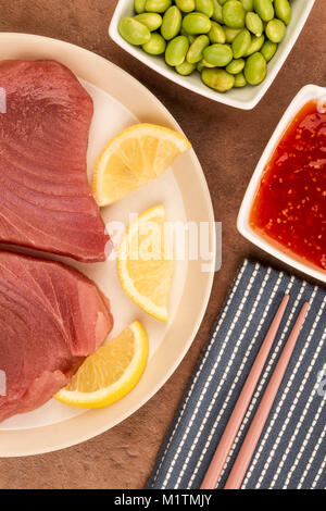 Frisches Rohes ungekocht Gelbflossenthun Steaks mit Zitronenscheiben auf rotem Hintergrund Stockfoto