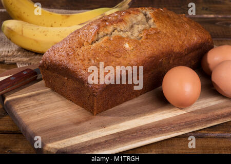 Laib Bananen-nuss süßes Brot und braunen ei Zutat auf einer hölzernen Schneidebrett Stockfoto