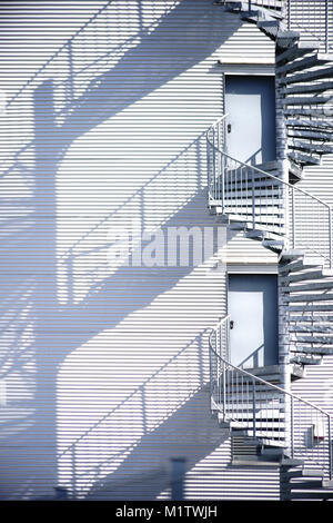 Eine Wendeltreppe, Feuerleiter an der Seite eines industriellen Fassade wirft Schatten. Stockfoto