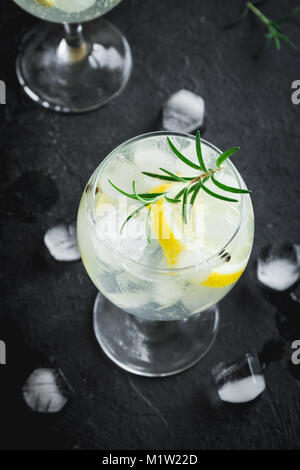 Alkohol trinken (Gin Tonic Cocktail) mit Zitrone, Rosmarin und Eis auf rustikalen schwarzen Stein Tabelle, Kopieren, Ansicht von oben. Iced Drink mit Zitrone und Kräutern. Stockfoto