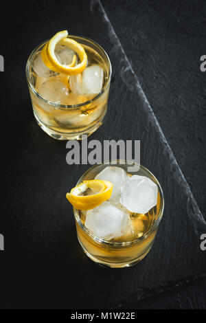 Whiskey on the rocks mit Zitronenschale. Whisky mit Eis, garniert mit Citrus Twist auf schwarzem Stein serviert, Ansicht von oben, kopieren. Stockfoto