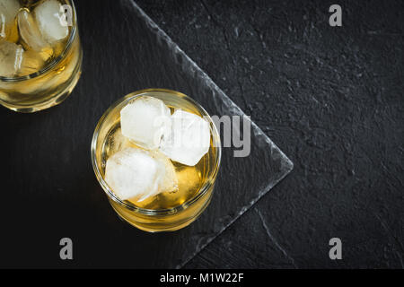 Whiskey on the rocks mit Zitronenschale. Whisky mit Eis, garniert mit Citrus Twist auf schwarzem Stein serviert, Ansicht von oben, kopieren. Stockfoto