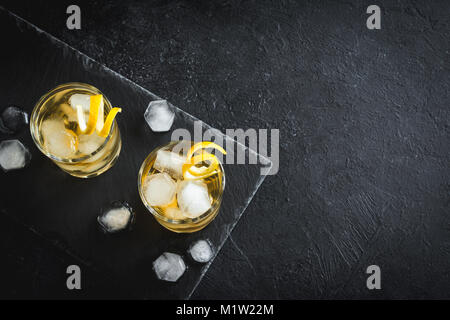 Whiskey on the rocks mit Zitronenschale. Whisky mit Eis, garniert mit Citrus Twist auf schwarzem Stein serviert, Ansicht von oben, kopieren. Stockfoto