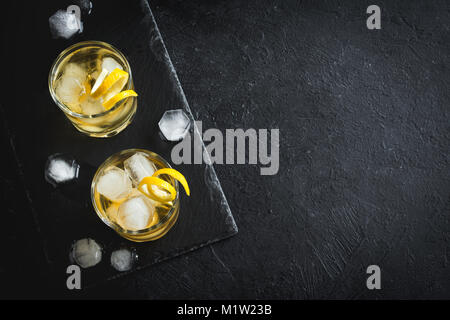 Whiskey on the rocks mit Zitronenschale. Whisky mit Eis, garniert mit Citrus Twist auf schwarzem Stein serviert, Ansicht von oben, kopieren. Stockfoto