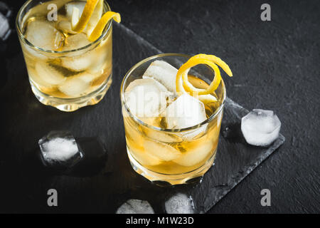 Whiskey on the rocks mit Zitronenschale. Whisky mit Eis, garniert mit Citrus Twist auf schwarzem Stein serviert, Ansicht von oben, kopieren. Stockfoto