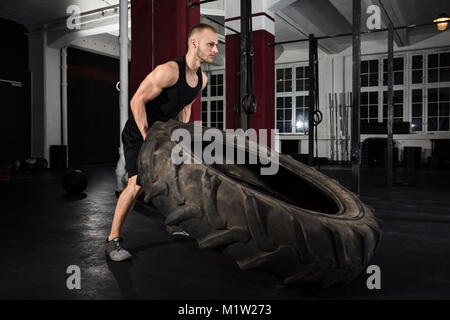 Junge Athlet Mann Drücken LKW-Reifen in der Turnhalle Stockfoto