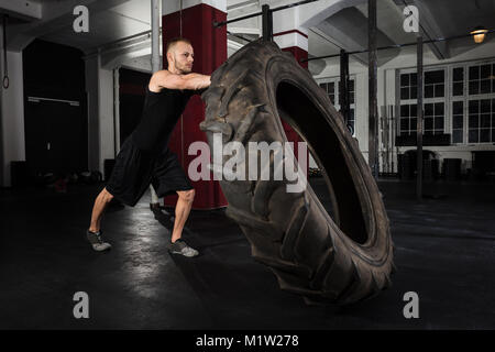 Junge Athlet Mann Drücken LKW-Reifen in der Turnhalle Stockfoto