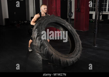 Junge Athlet Mann Drücken LKW-Reifen in der Turnhalle Stockfoto