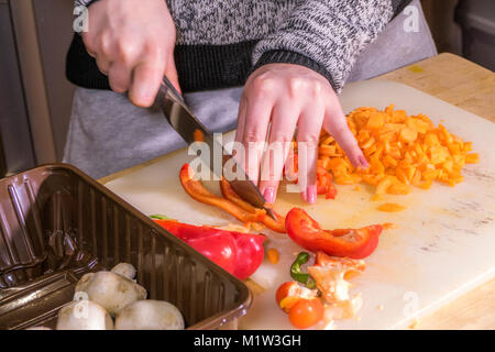 Eine Frau (nur Hände) hacken ein roter Pfeffer auf einem Brett mit einem großen, scharfen, Edelstahl Messer, mit anderen Gemüse in der Nähe. UK. Stockfoto