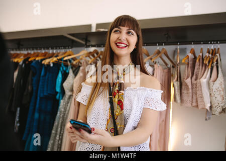 Glückliche Kunden der Eingabe der PIN am Point of sale Maschine in eine Boutique. Vielzahl von Designer Kleidung auf Anzeige an eine Mode Kleidung kaufen. Stockfoto