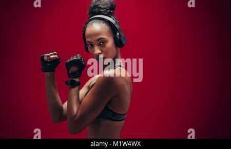 Selbstbewussten jungen Frau mit Kopfhörer in eine Kampfstellung stehen. Schöne und passende Frau bereit für Ihr Workout auf roten Hintergrund. Stockfoto