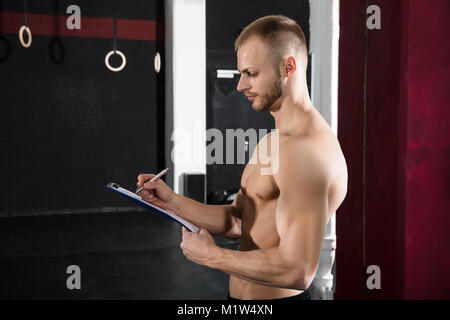 Nahaufnahme einer Person Hand Schreiben ein Workout Plan über die Zwischenablage In der Turnhalle Stockfoto