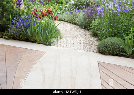 Moderne, zeitgenössische Holzterrasse mit Terrasse und gebogenem Schottergartenweg, der durch einen wilden Garten führt, Chelsea Flower Show UK Stockfoto