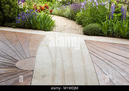 Moderne, zeitgenössische Holzterrasse mit Terrasse und gebogenem Schottergartenweg, der durch einen wilden Garten führt, Chelsea Flower Show UK Stockfoto