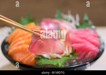 Stäbchen mit Hamachi Sashimi mit gemischten geschnittenen Fisch sashimi auf Eis im schwarzen Schüssel. Sashimi Lachs Thunfisch Hamachi Garnelen und Surf Ruhig, roher Fisch, ja Stockfoto