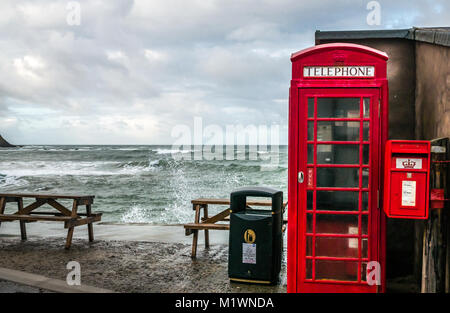 Pennan, Aberdeenshire, Schottland, Vereinigtes Königreich. Die starken Winde erzeugen eine Welle in der Nordsee entlang der Nordostküste Schottlands, mit großen Wellen, die gegen die Promenade in dem malerischen Dorf plätschern, das berühmt ist für seinen Film Local Hero. Die ikonische britische rote Telefonbox, ursprünglich eine Filmrequisite, wurde später als Folge der öffentlichen Nachfrage installiert Stockfoto