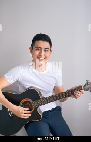 Schönen asiatischen Mann spielt auf der Gitarre, auf der Couch zu Hause Stockfoto