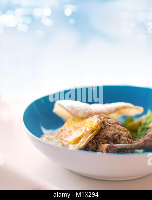 Gebratener Reis mit Huhn. Eine Schüssel mit gebratener Reis auf die Stimmung blau bokeh Hintergrund mit sunny side up Ei, drumstick Huhn und Garnelen Crackers serviert. Stockfoto