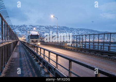 Ein Lkw kreuze Tromsø-Brücke in Tromsø, Norwegen, mitten im polaren Winter, mit Schnee Berge im Hintergrund. Stockfoto