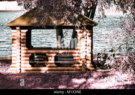 Am Ufer des Flusses in den Schatten der Bäume, ein Pavillon aus Baumstämmen und mit Schindeln gedeckt. Die Wirkung von Infrarot Film. Stockfoto