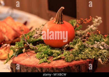 Kürbis und Gemüse als Dekoration auf einem Baumstumpf im Restaurant. Halloween Dekoration mit einem frischen Kürbis und Gemüse im Vintage Style. Stockfoto