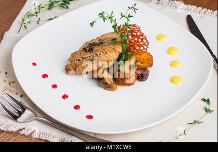 Gebackener Fisch mit Kartoffeln und Pilze auf eine weisse Platte Stockfoto