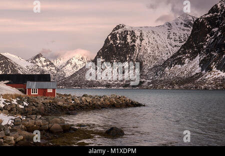 Eine rote Fischerhütte und schneebedeckten Landschaft, die von der E10 Flakstadøya auf den Lofoten in Norwegen Stockfoto