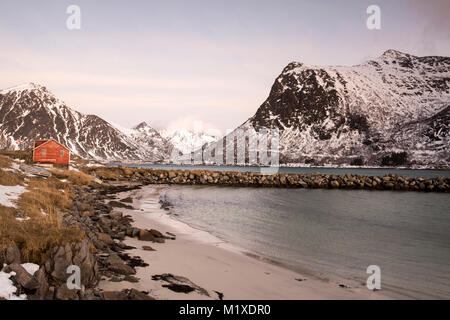 Eine rote Fischerhütte und schneebedeckten Landschaft, die von der E10 Flakstadøya auf den Lofoten in Norwegen Stockfoto