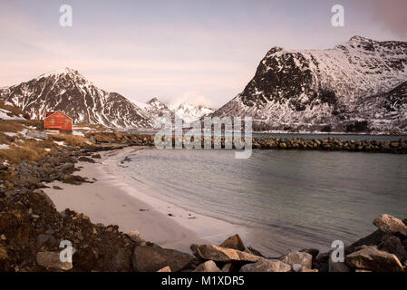 Eine rote Fischerhütte und schneebedeckten Landschaft, die von der E10 Flakstadøya auf den Lofoten in Norwegen Stockfoto