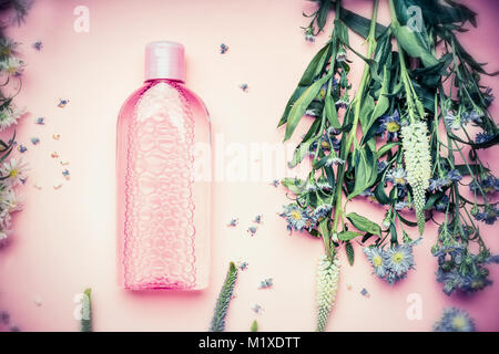 Plastikflasche mit Tonic oder Micellares reinigende Wasser mit frischen Kräutern und Blumen auf rosa Hintergrund, Ansicht von oben. Schönheit, Haut, Haare oder Körperpflege conc Stockfoto