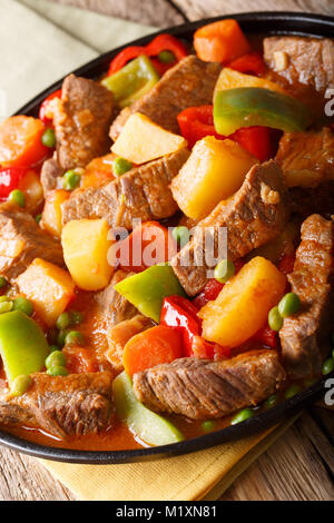 Eintopf mit Rindfleisch, Kartoffeln, Paprika, Erbsen, Tomaten und Karotten closeup auf einem Teller auf den Tisch. Vertikale Stockfoto