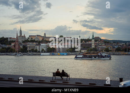 Die liebende Paar ist auf der Bank sitzen und genießen Sie die Landschaft des Flusses Danuve in Budapest, Ungarn während des Sonnenuntergangs. Stockfoto