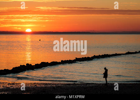 Ein Wanderer genießen Sie den Sonnenaufgang am Strand in Dorset Stockfoto