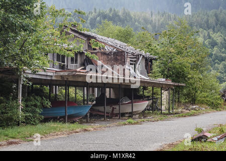 Mit Obstbäumen daneben und Boote und Trailer noch in den Carport, ein verlassenes Haus steht in Ruinen in der Geisterstadt Ozean fällt, BC. Stockfoto