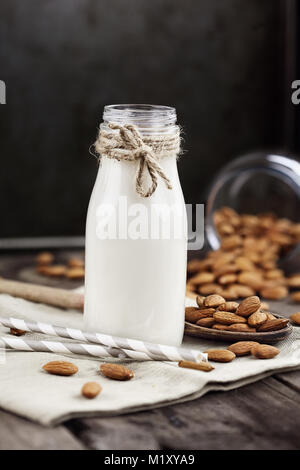 Organische weiße Mandelmilch in einer Glasflasche mit ganzen Mandeln über einen rustikalen Holztisch verschüttet. Stockfoto