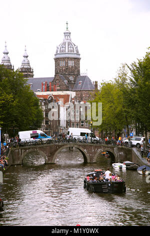 AMSTERDAM, NIEDERLANDE - 19 AUGUST 2015: Blick auf Sankt Nikolaus Kirche oder St Nicolaas kerk Turm aus Oudekennissteeg Brücke. Das Leben auf der Straße, Kanal, Stockfoto