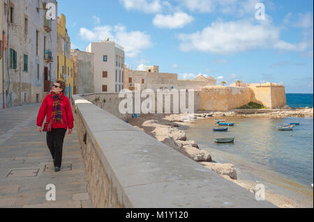 Frau solo Tourist allein Konzept, Blick auf eine reife Frau Reisende zu Fuß entlang der Meeresmauer am Nordufer von Trapani, Sizilien. [MODELL FREIGEGEBEN] Stockfoto